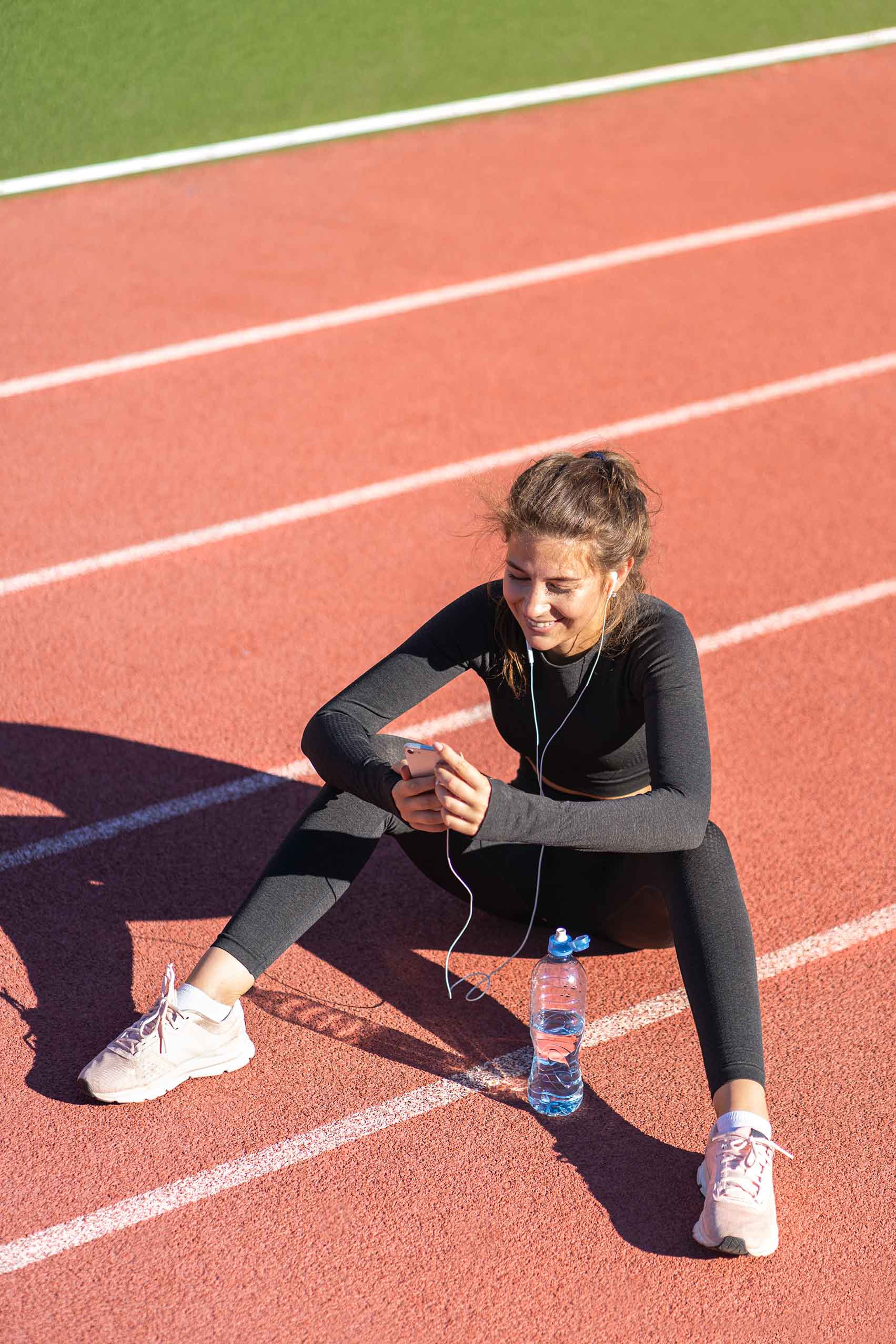Atleta sentada con teléfono y botella.
